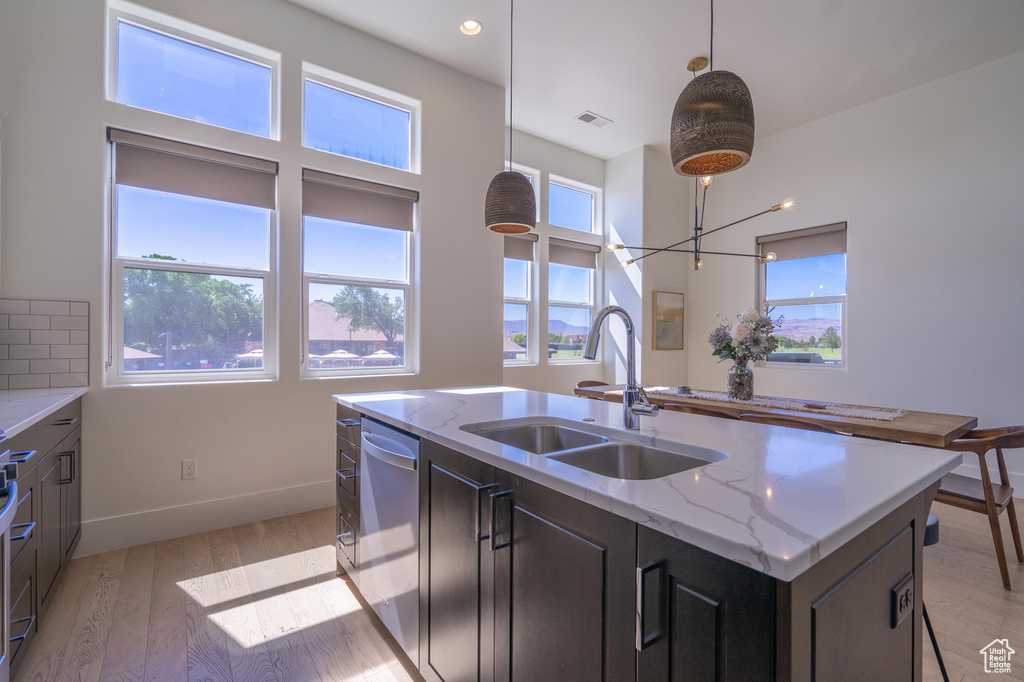 Kitchen with stainless steel dishwasher, a sink, light wood finished floors, a kitchen island with sink, and decorative light fixtures
