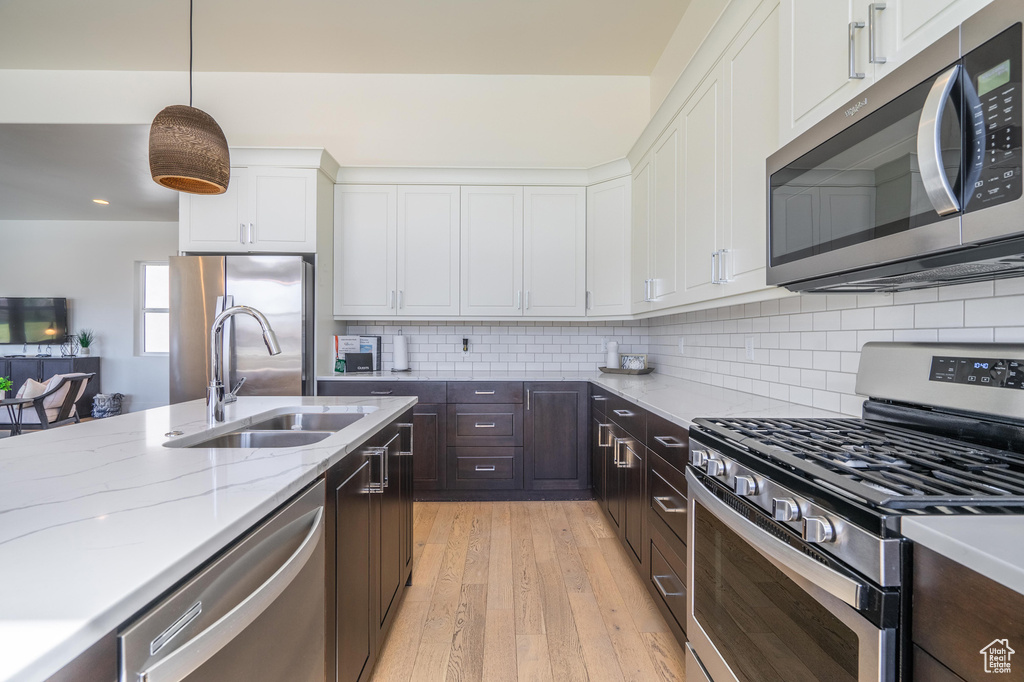 Kitchen featuring appliances with stainless steel finishes, a sink, white cabinets, light wood-style flooring, and dark brown cabinets