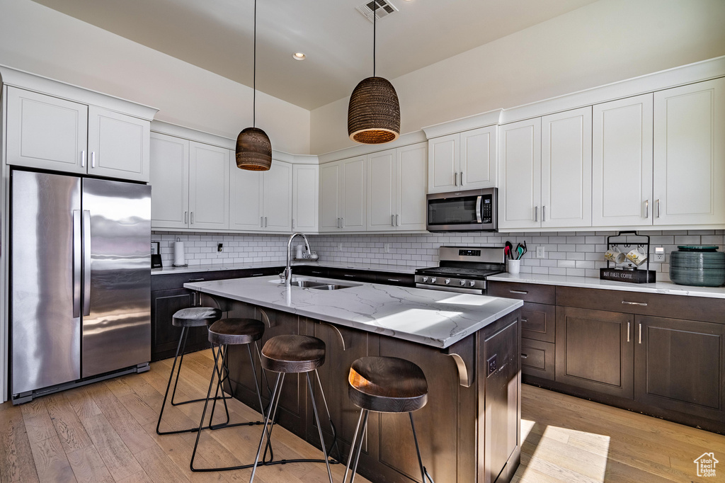 Kitchen featuring appliances with stainless steel finishes, a sink, light wood finished floors, a kitchen island with sink, and recessed lighting