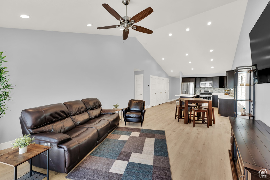Living area with high vaulted ceiling, light wood-type flooring, ceiling fan, recessed lighting, and baseboards