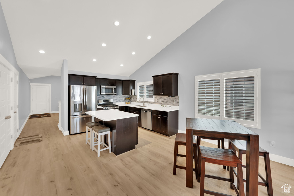 Kitchen featuring appliances with stainless steel finishes, a sink, a kitchen island, light countertops, and light wood-type flooring