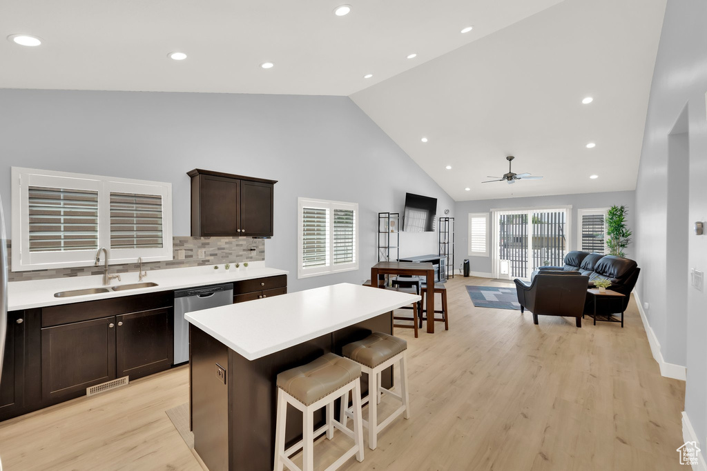 Kitchen with a sink, stainless steel dishwasher, high vaulted ceiling, dark brown cabinetry, and light countertops
