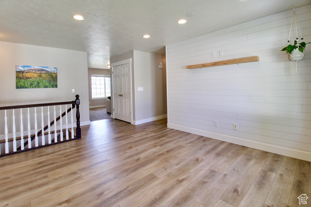 Unfurnished room featuring baseboards, light wood finished floors, recessed lighting, and wood walls