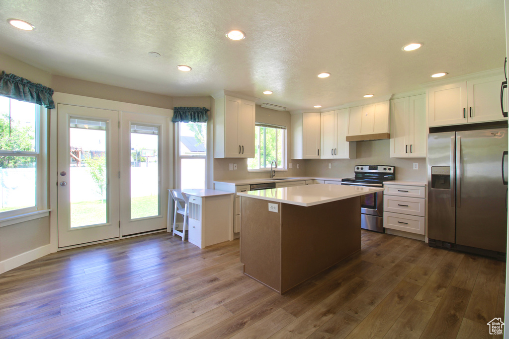 Kitchen with stainless steel appliances, a center island, light countertops, dark wood-style flooring, and white cabinetry