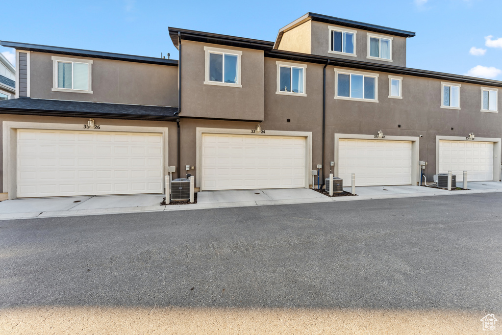 View of front of house with stucco siding, central AC unit, and an attached garage