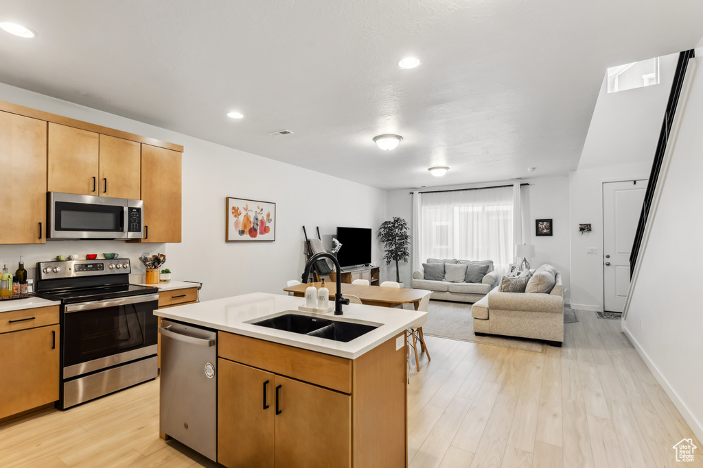 Kitchen featuring stainless steel appliances, a sink, light countertops, light wood-style flooring, and an island with sink