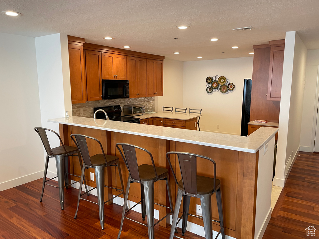 Kitchen with black appliances, a peninsula, brown cabinetry, dark wood-style floors, and backsplash