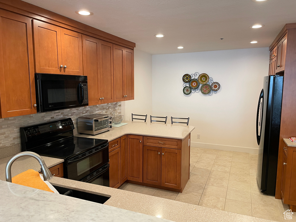Kitchen featuring black appliances, tasteful backsplash, recessed lighting, brown cabinetry, and a peninsula