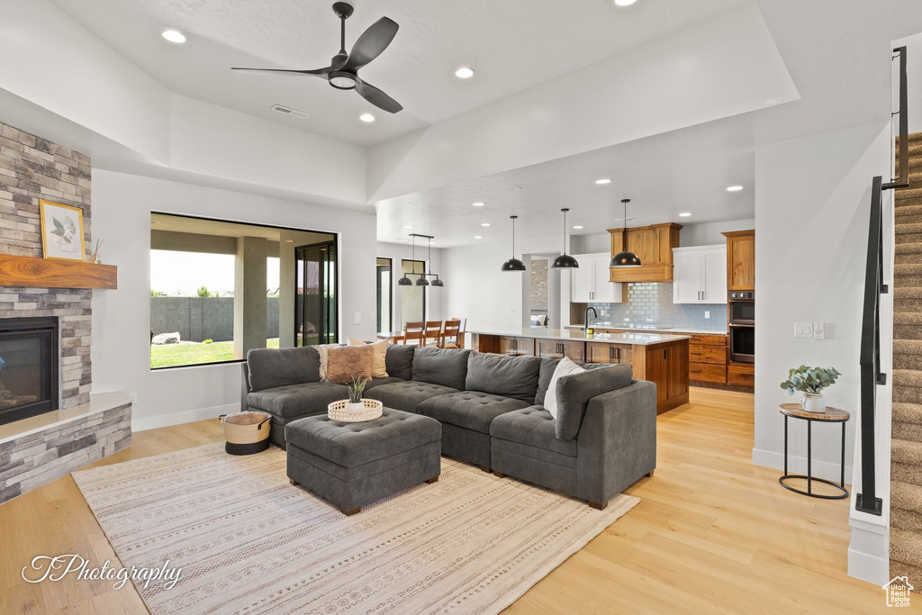 Living room with stairway, a ceiling fan, light wood-type flooring, recessed lighting, and a fireplace