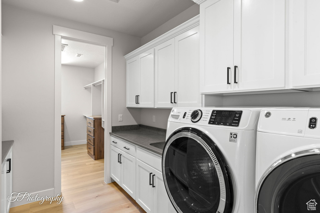 Laundry area with washer and dryer, cabinet space, light wood-type flooring, and baseboards