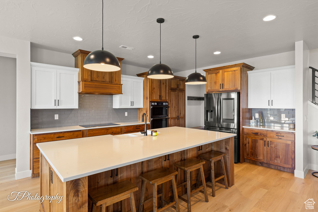 Kitchen with black appliances, a sink, light wood-style floors, light countertops, and a kitchen breakfast bar