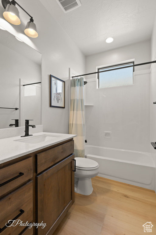 Full bath with shower / bath combo, vanity, wood finished floors, and toilet