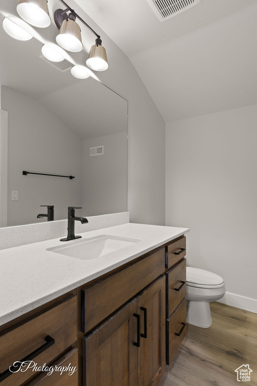 Bathroom with lofted ceiling, vanity, toilet, wood finished floors, and baseboards