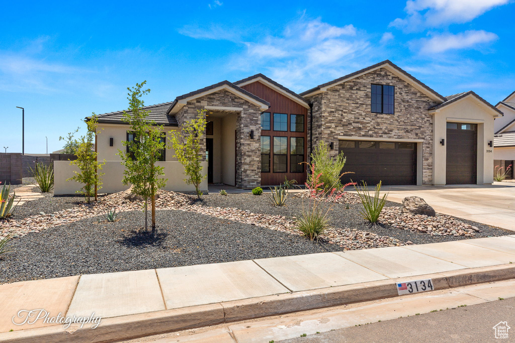 View of front of property with stone siding, an attached garage, stucco siding, driveway, and a tiled roof