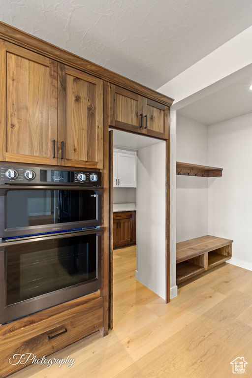 Kitchen with multiple ovens, light wood-style flooring, baseboards, and brown cabinets