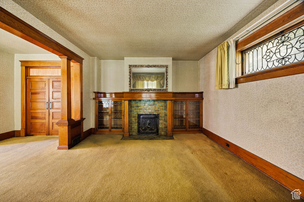 Unfurnished living room with carpet flooring, baseboards, ornate columns, and a textured ceiling