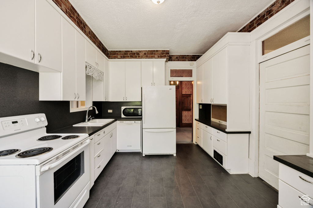 Kitchen featuring white appliances, a sink, a textured ceiling, dark countertops, and white cabinets