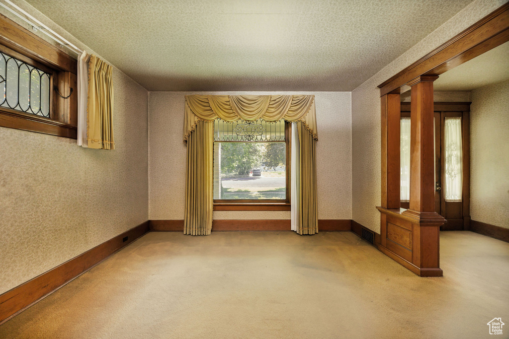 Empty room featuring ornate columns, carpet, a textured ceiling, and baseboards