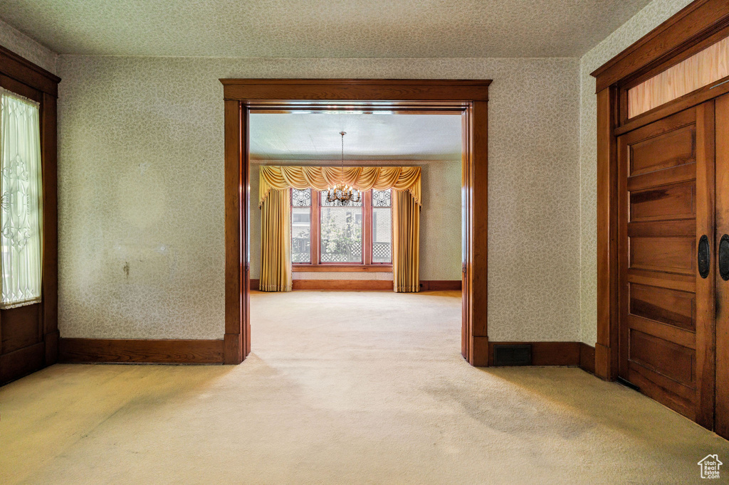 Corridor featuring a chandelier, wallpapered walls, light colored carpet, and baseboards