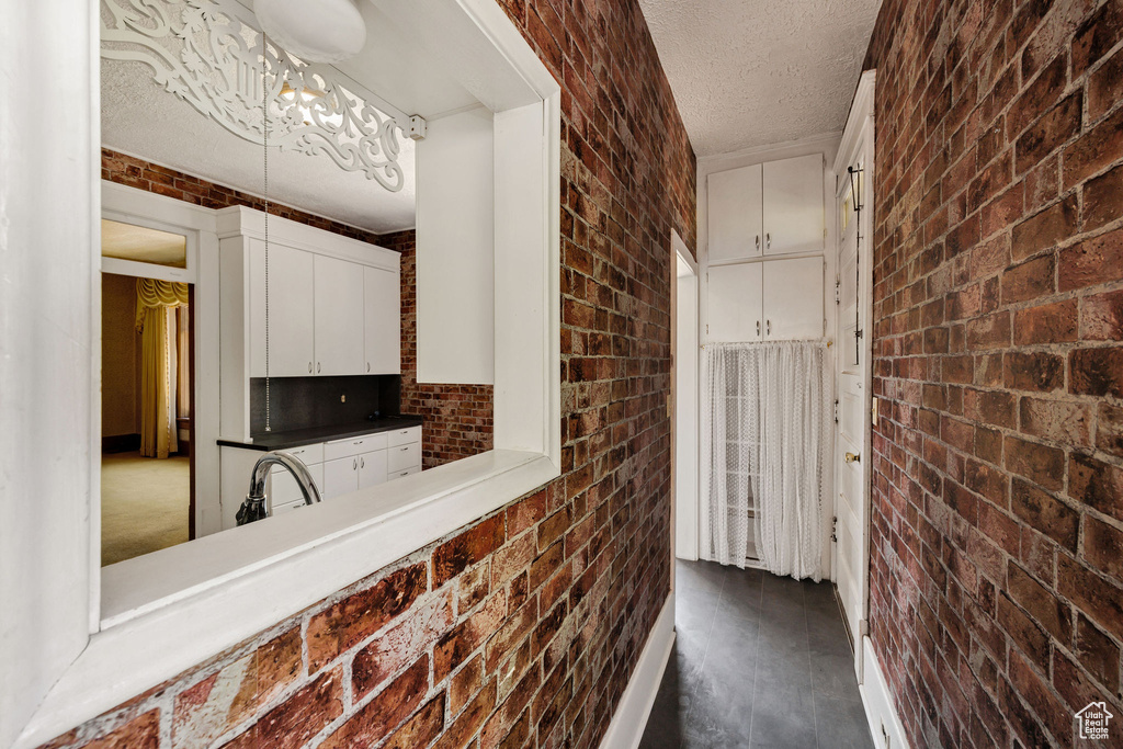 Kitchen featuring brick wall, a textured ceiling, white cabinetry, a sink, and dark wood-style floors
