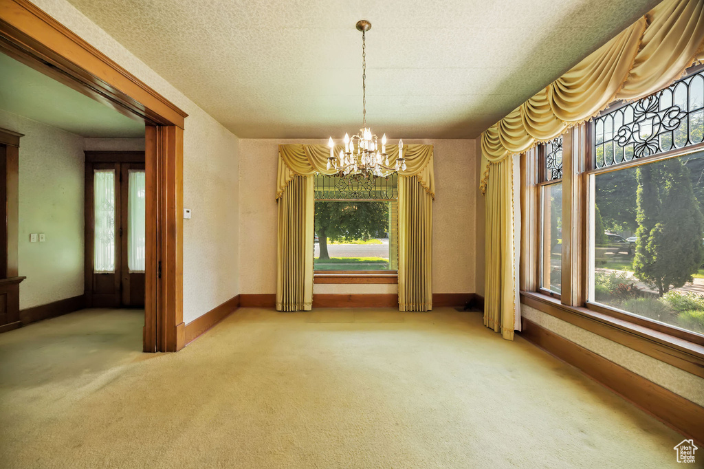 Unfurnished dining area with a chandelier, healthy amount of natural light, and carpet flooring