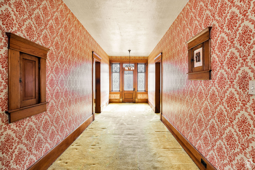 Hallway featuring wallpapered walls, baseboards, and light colored carpet