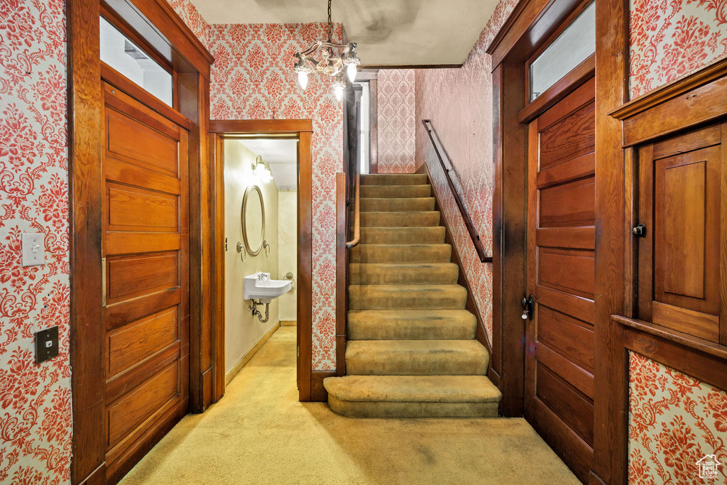 Stairway featuring wallpapered walls, carpet flooring, a chandelier, and baseboards