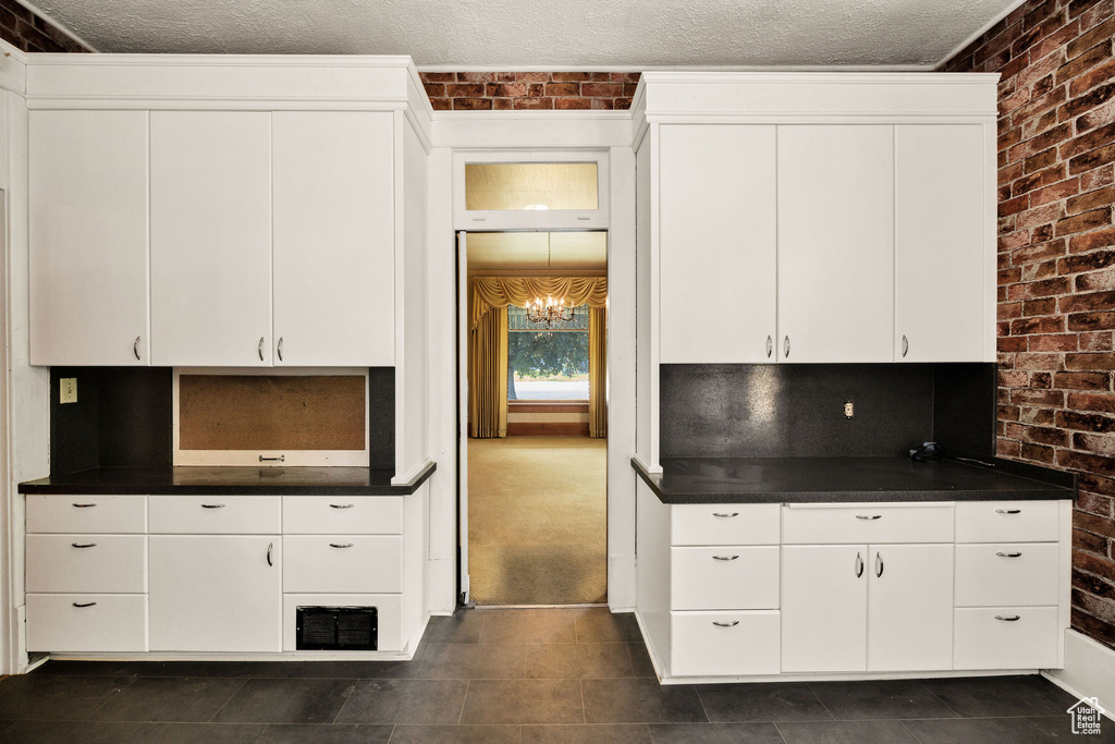 Kitchen with brick wall, dark countertops, white cabinets, dark tile patterned floors, and a textured ceiling