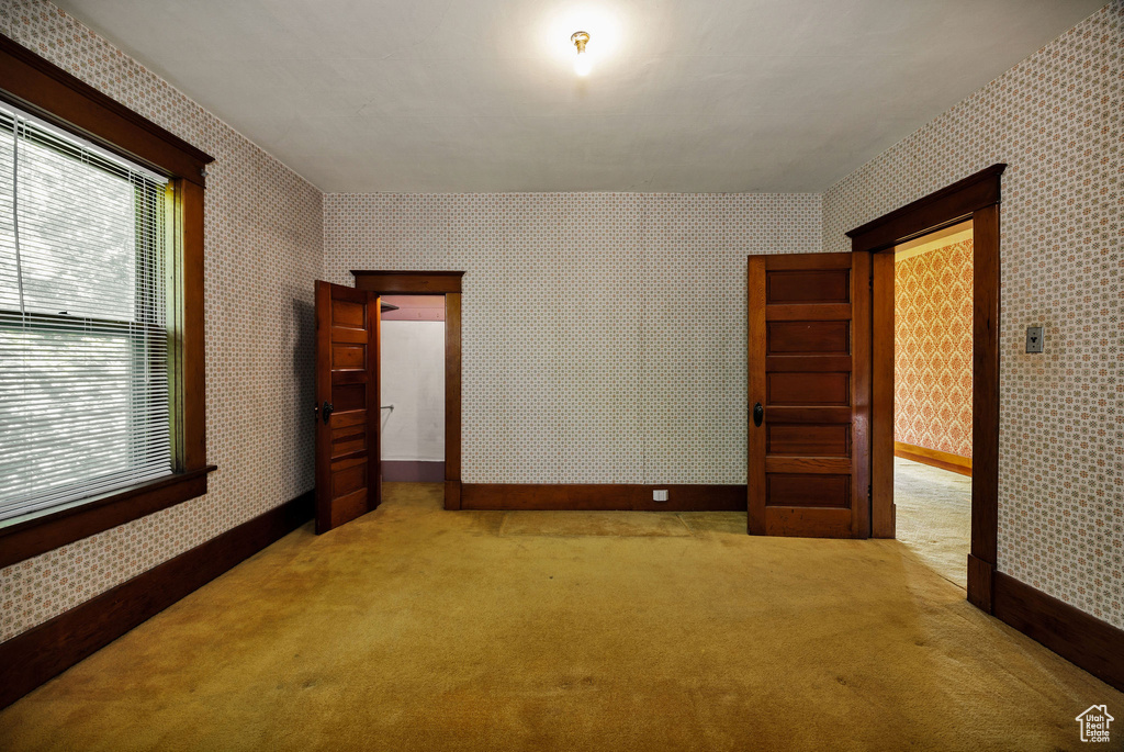 Carpeted empty room with wallpapered walls, healthy amount of natural light, and baseboards