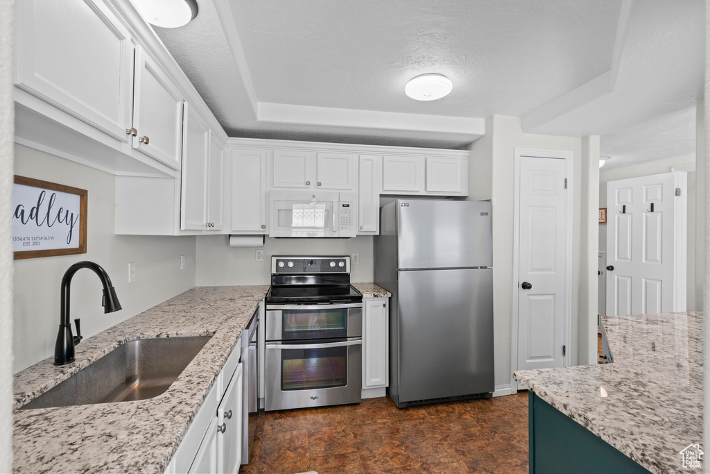 Kitchen featuring stainless steel appliances, a sink, white cabinets, and light stone counters