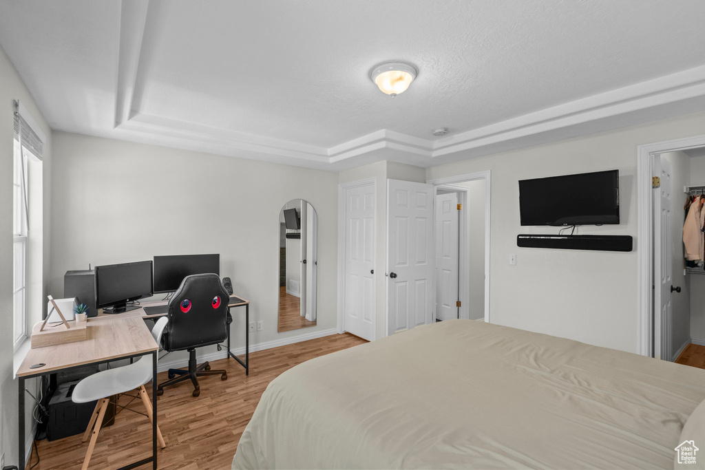 Bedroom with a tray ceiling, arched walkways, wood finished floors, baseboards, and an office area