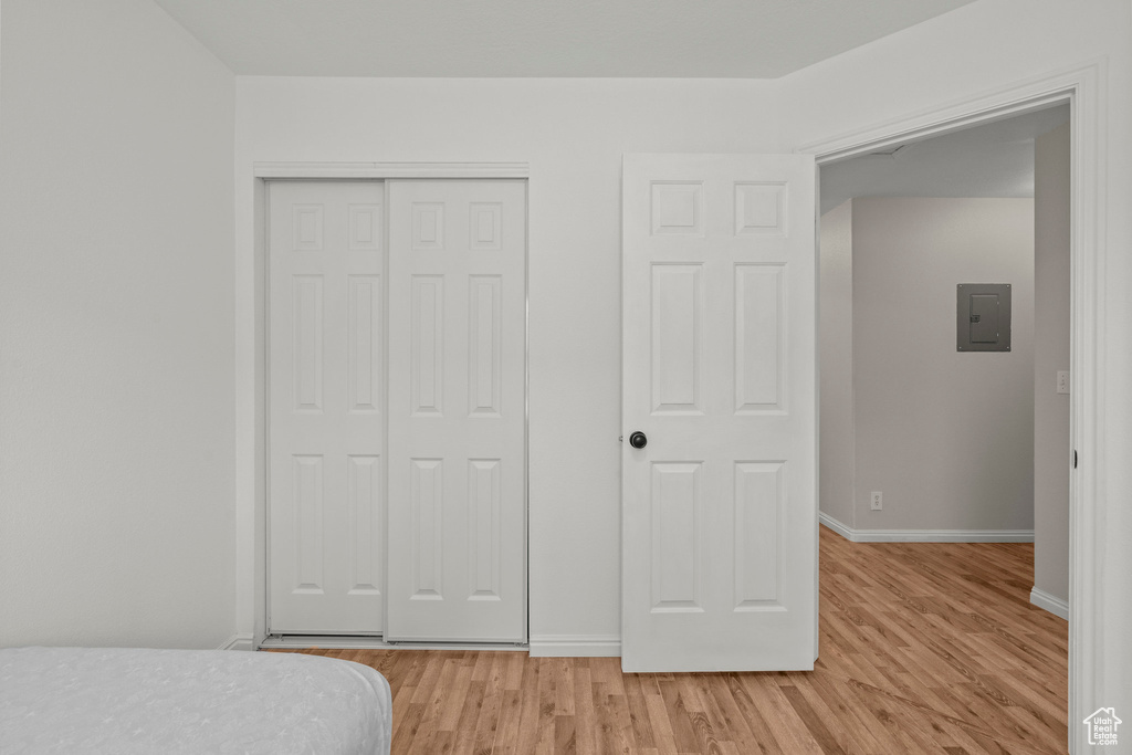 Bedroom featuring a closet, light wood-style floors, baseboards, and electric panel