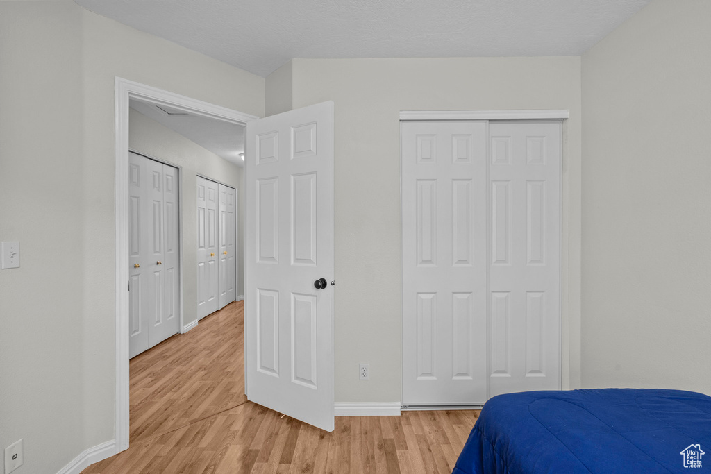 Bedroom with light wood-style floors, baseboards, and multiple closets
