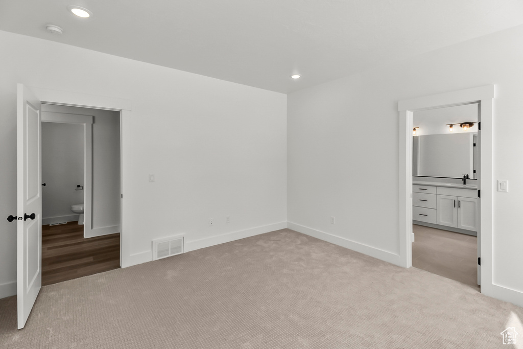 Unfurnished bedroom featuring light colored carpet, recessed lighting, a sink, connected bathroom, and baseboards