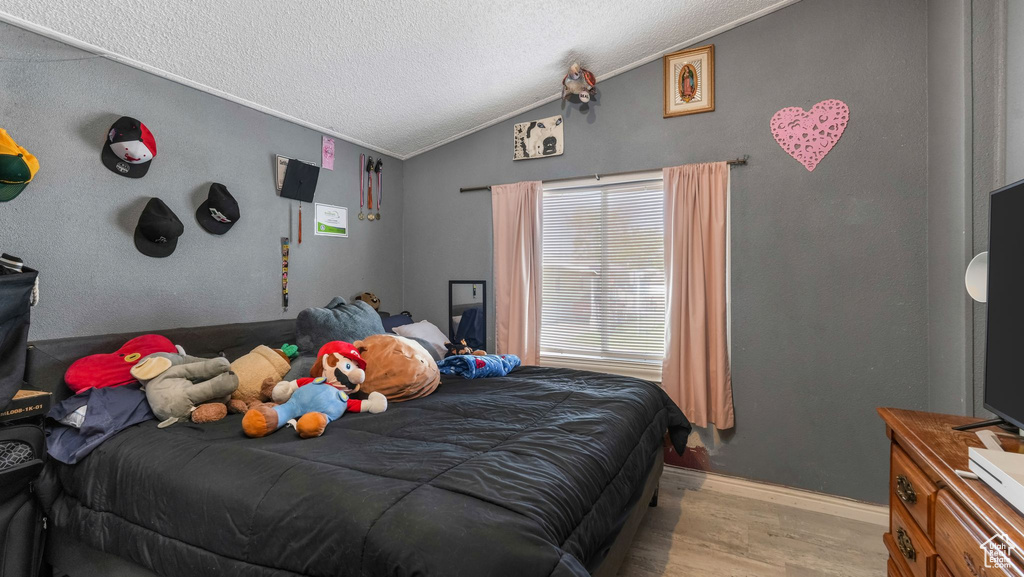 Bedroom with light wood-style floors, lofted ceiling, a textured ceiling, and ornamental molding