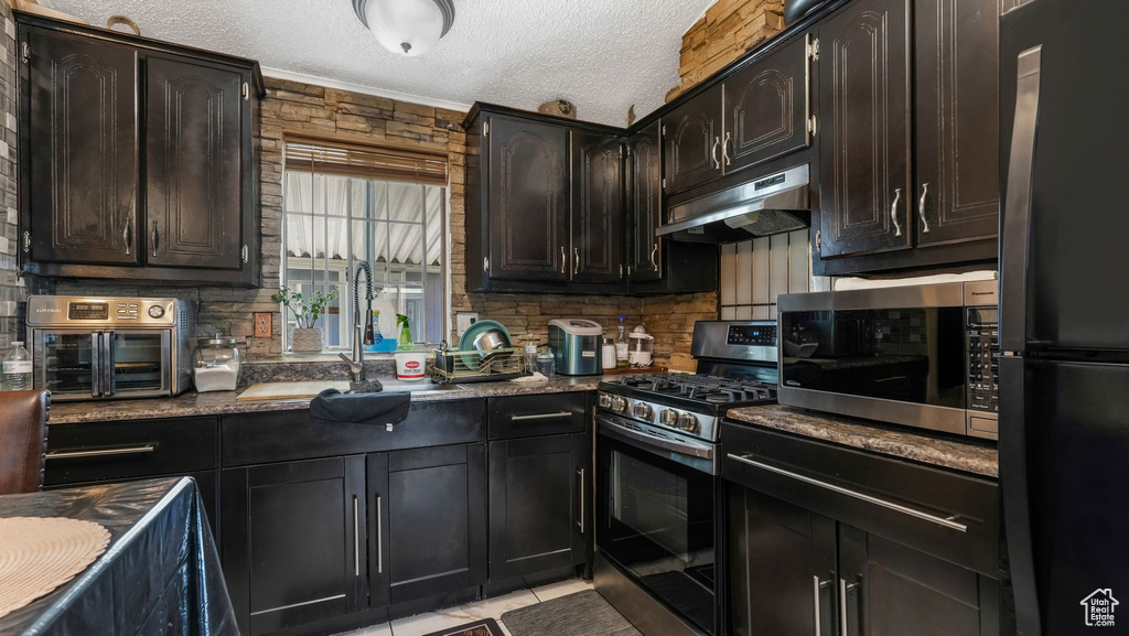 Kitchen featuring appliances with stainless steel finishes, under cabinet range hood, backsplash, a textured ceiling, and a sink