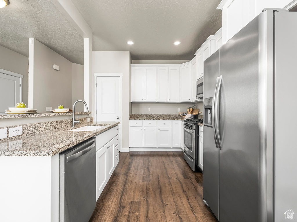 Kitchen featuring appliances with stainless steel finishes, a sink, dark wood finished floors, white cabinets, and light stone counters