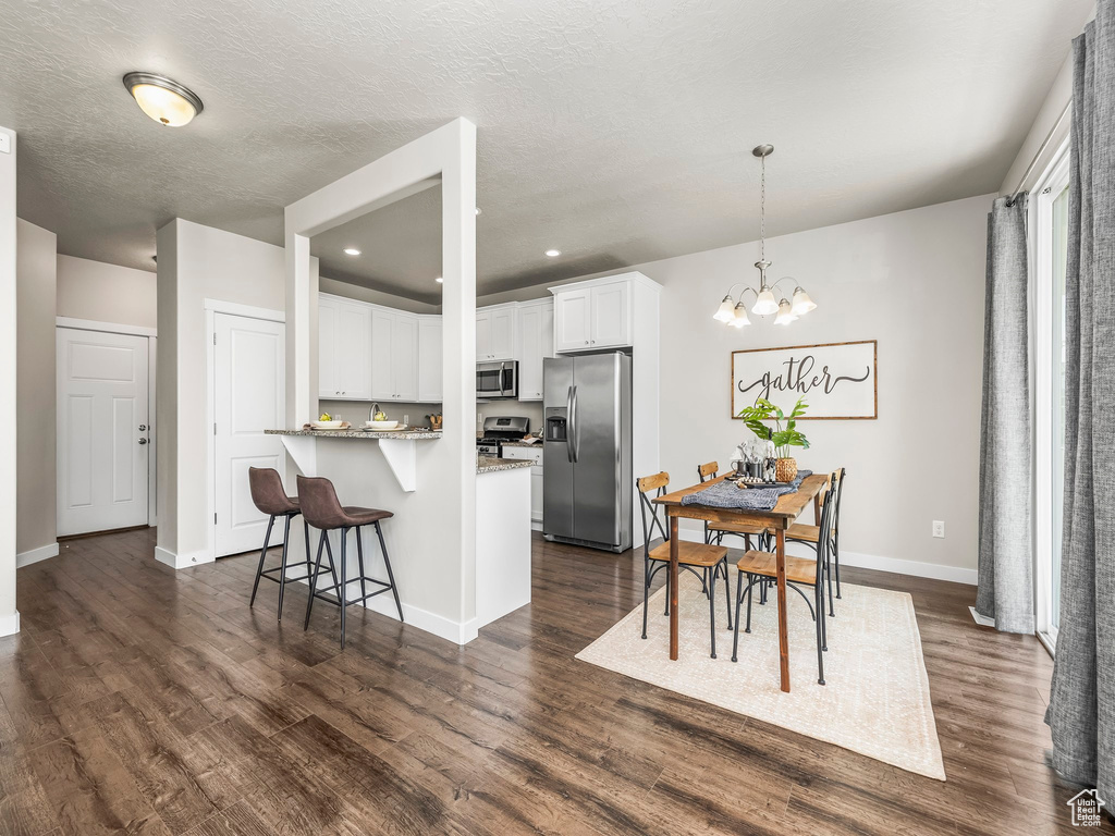 Kitchen with stainless steel appliances, dark wood finished floors, a breakfast bar area, white cabinetry, and recessed lighting