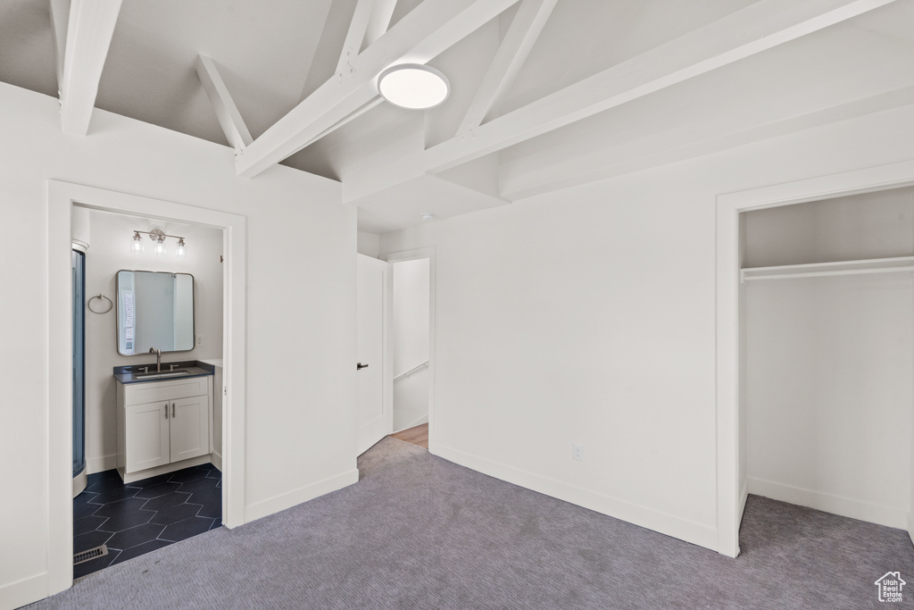 Unfurnished bedroom with a sink, dark carpet, a closet, ensuite bathroom, and baseboards