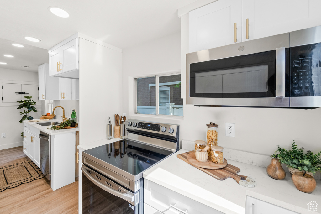 Kitchen featuring stainless steel appliances, a sink, light wood finished floors, white cabinetry, and light countertops