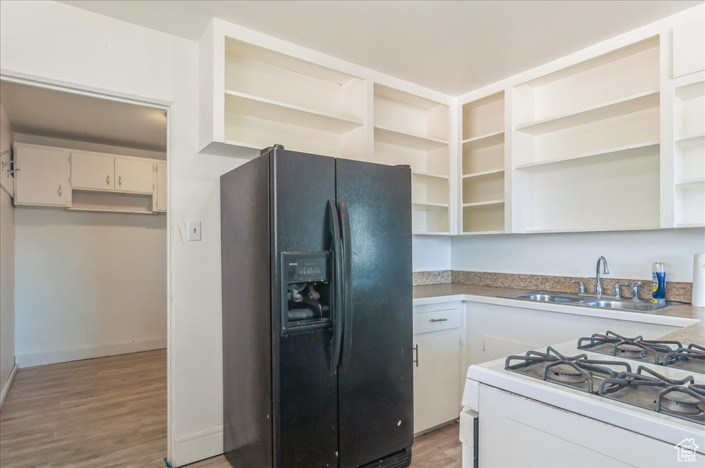 Kitchen featuring black fridge with ice dispenser, open shelves, a sink, white range with gas cooktop, and white cabinets