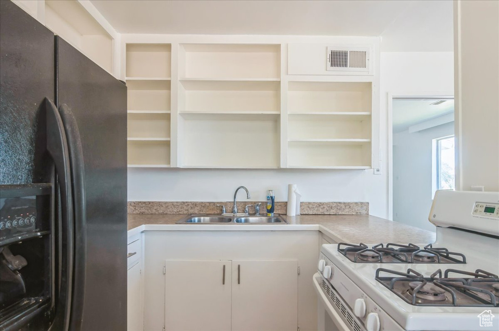 Kitchen featuring black fridge, white gas range oven, open shelves, and a sink