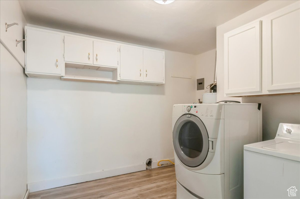 Laundry room featuring light wood finished floors, washing machine and clothes dryer, cabinet space, and baseboards