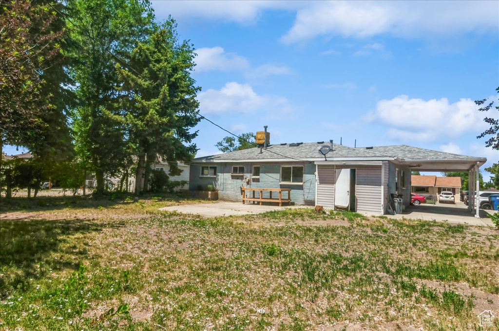Back of property with an attached carport, a patio, and a yard