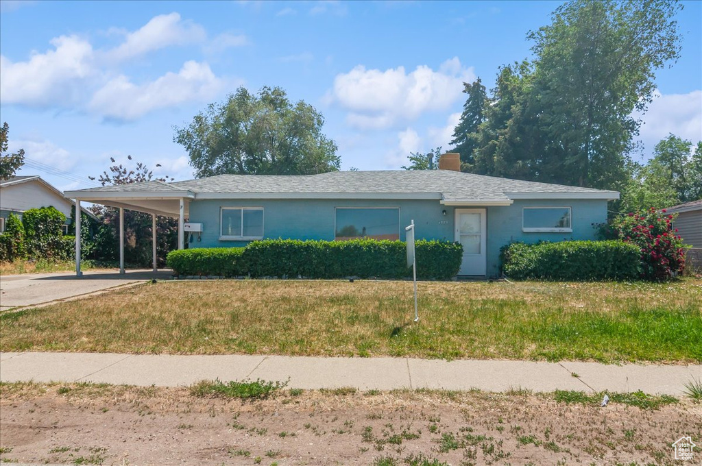Ranch-style home with a front lawn, a chimney, an attached carport, stucco siding, and driveway