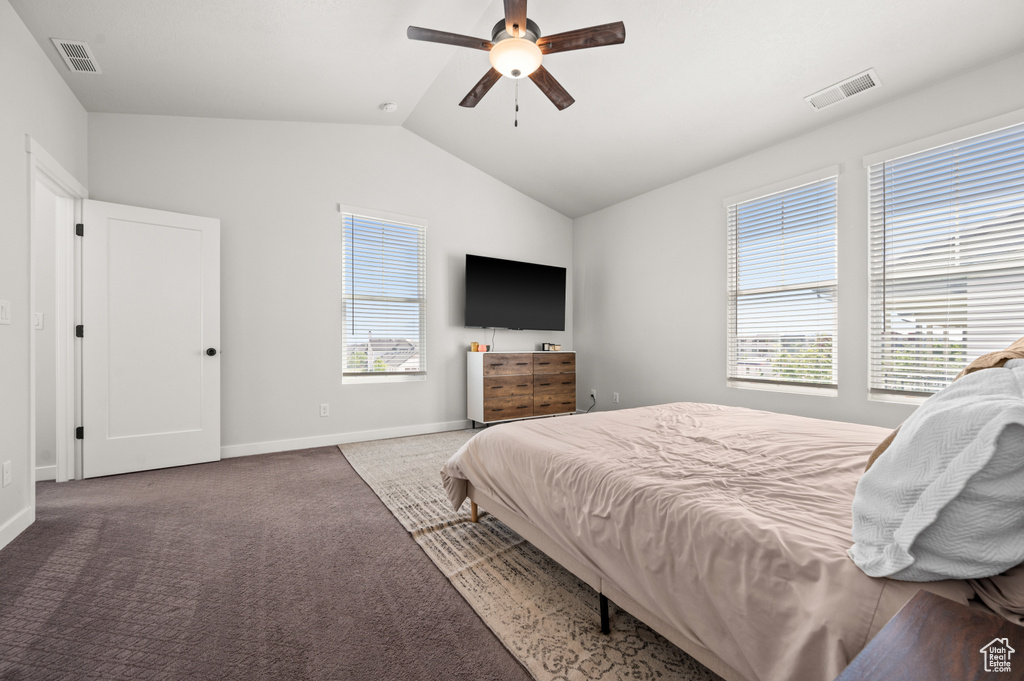 Carpeted bedroom featuring multiple windows, vaulted ceiling, baseboards, and ceiling fan