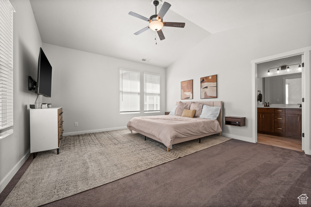 Bedroom with dark carpet, vaulted ceiling, baseboards, ensuite bathroom, and ceiling fan