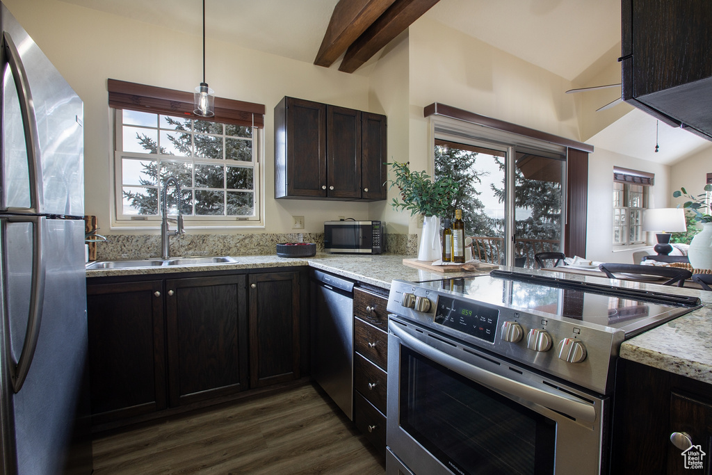Kitchen featuring appliances with stainless steel finishes, dark wood-style floors, light stone counters, a sink, and hanging light fixtures