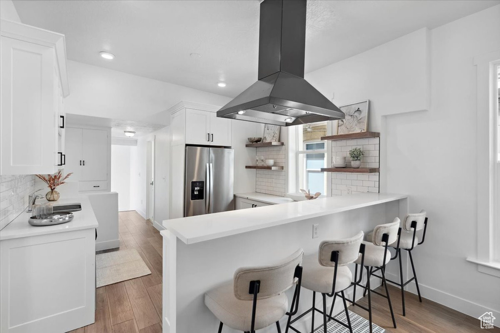 Kitchen with stainless steel fridge, island range hood, open shelves, tasteful backsplash, and white cabinetry