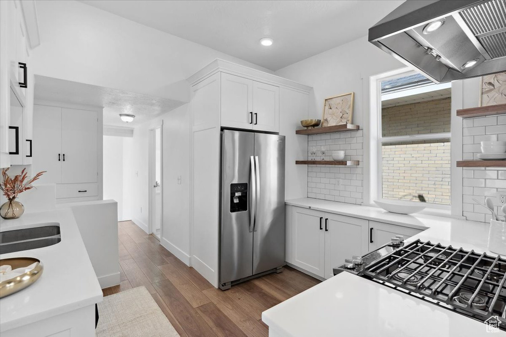Kitchen featuring stainless steel fridge, open shelves, ventilation hood, dark wood finished floors, and light countertops